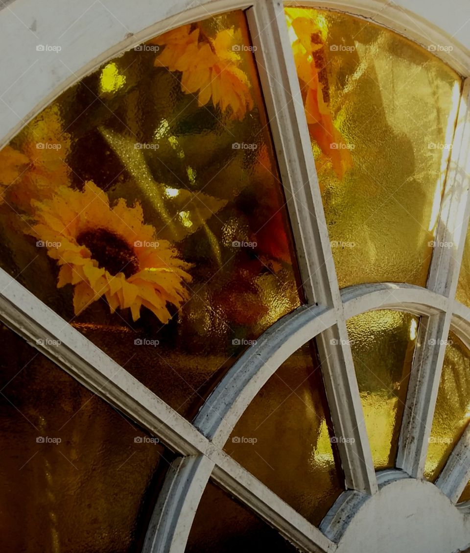 old leaded glass window with flower pot of sunflowers sitting in the window  amber glass colors of yellow green brown gold white arched window