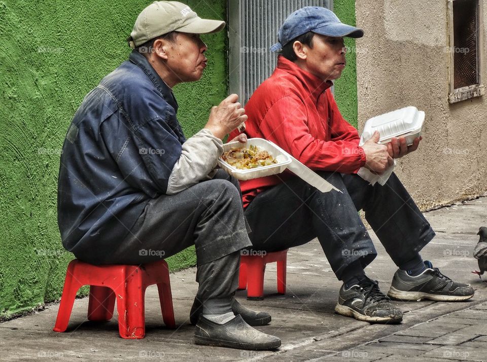 Pair Of Workers Eating Lunch In Chinatown. Workers Taking A Lunch Break In A Back Alley
