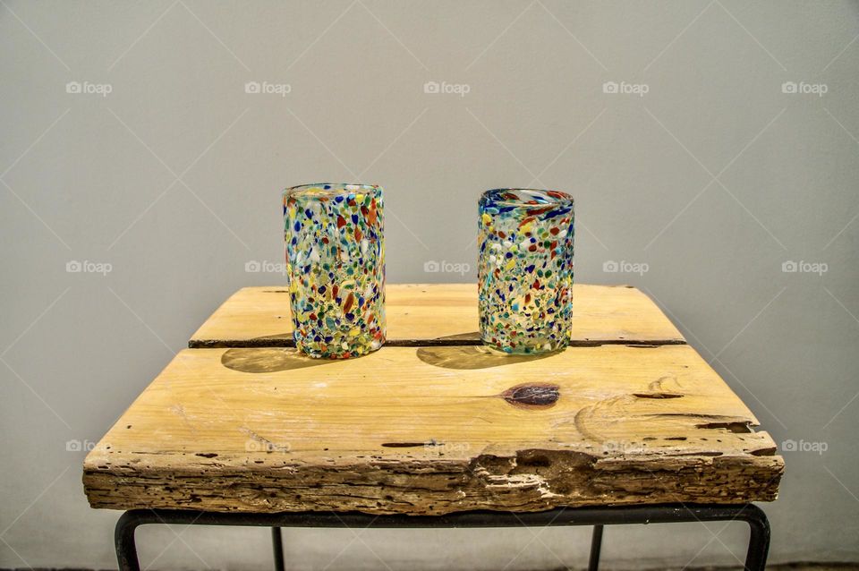 Two colourful recycled glasses on a repurposed wooden table.