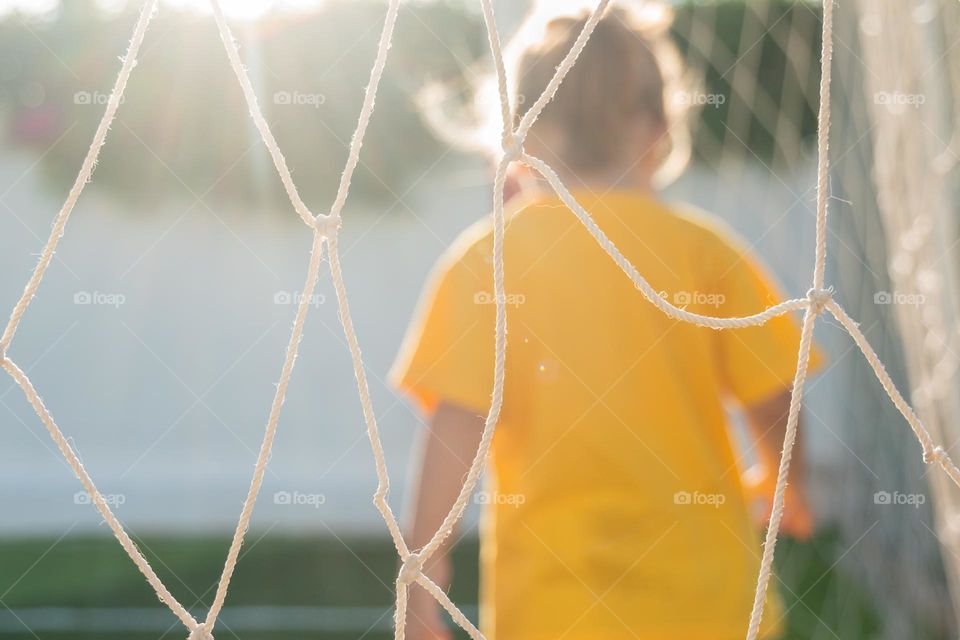 Back view of little girl through soccer goal net. Selective focus.