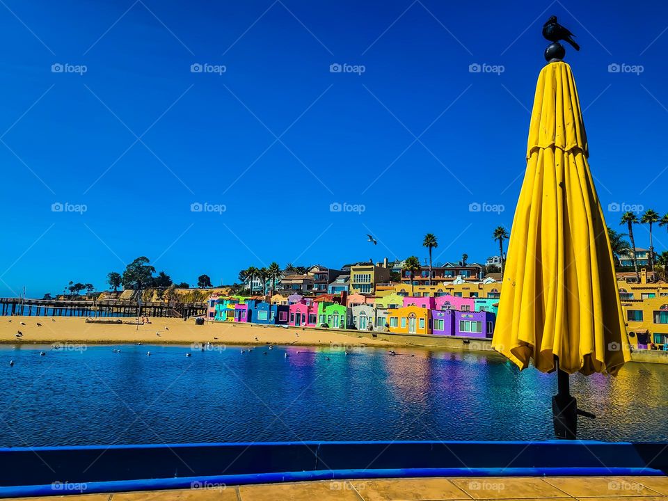 Sitting on a patio with an yellow umbrella with a blackbird perched on top on a warm summer afternoon in Capitola California with clear blue skies and the Venetian reflecting on the Soquel River with the warm sand of the beach.