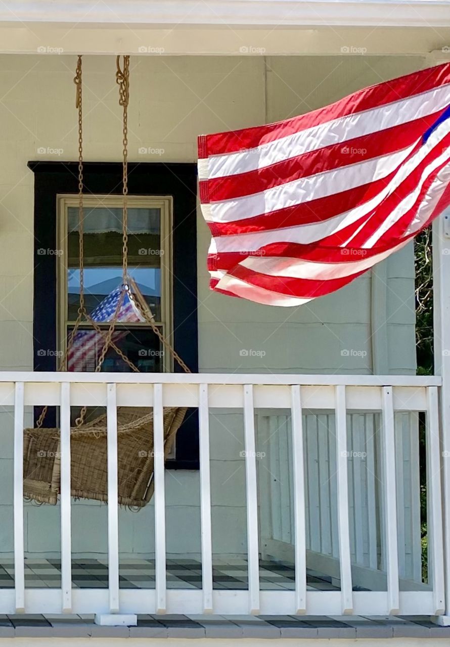 United States flag flying in the breeze on the porch of an old farm house 