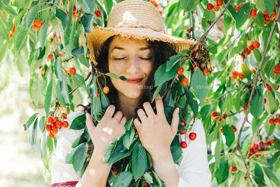 Young woman, being happy and smiling, while embracing the branches of a cherry tree, on a beautiful summer day.