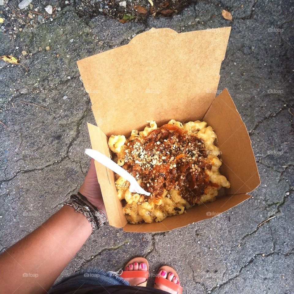 Mac and cheese being held by girl in orange sandals and jean shorts. Pittsburgh food truck Mac & Gold