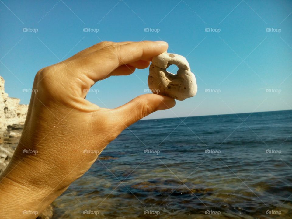 stone with hole in hand on the sea blue sky