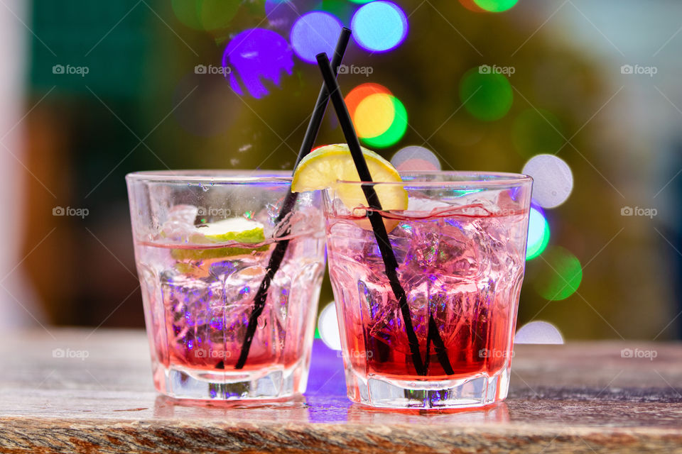 Delicious red cocktails in front of a beautiful festive green background with colorful bright lights. Black straws and lemon lime garnish. 