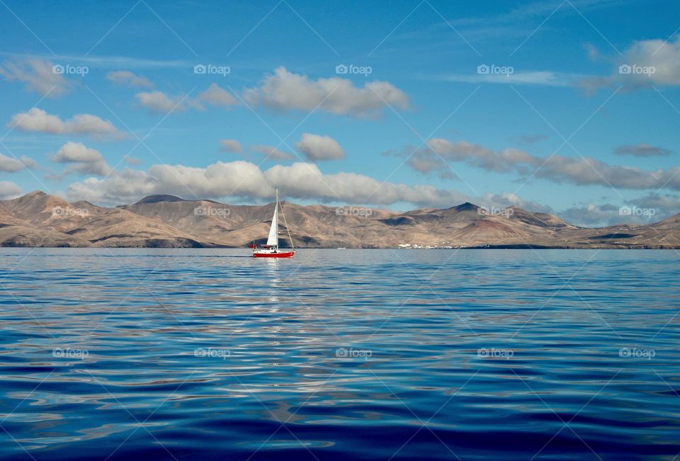 a red sailboat in the sea sailing along the coast of the island of Lanzarote, Canarias, Spain