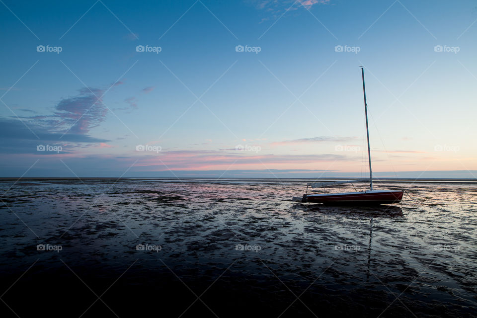 Very low tide in cape cod at sunrise with a sailboat