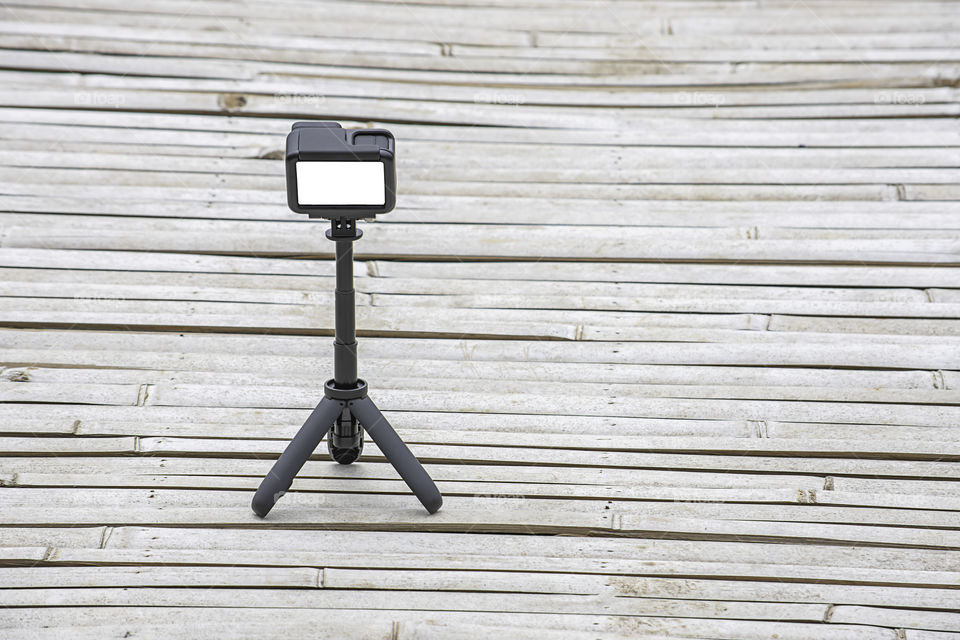 Camera and video with small black stand on a bamboo floor.