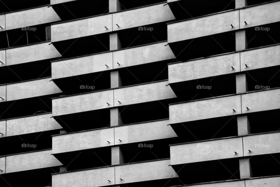 Black and white photo of pattern and regularity of a concrete skyscraper with balcony