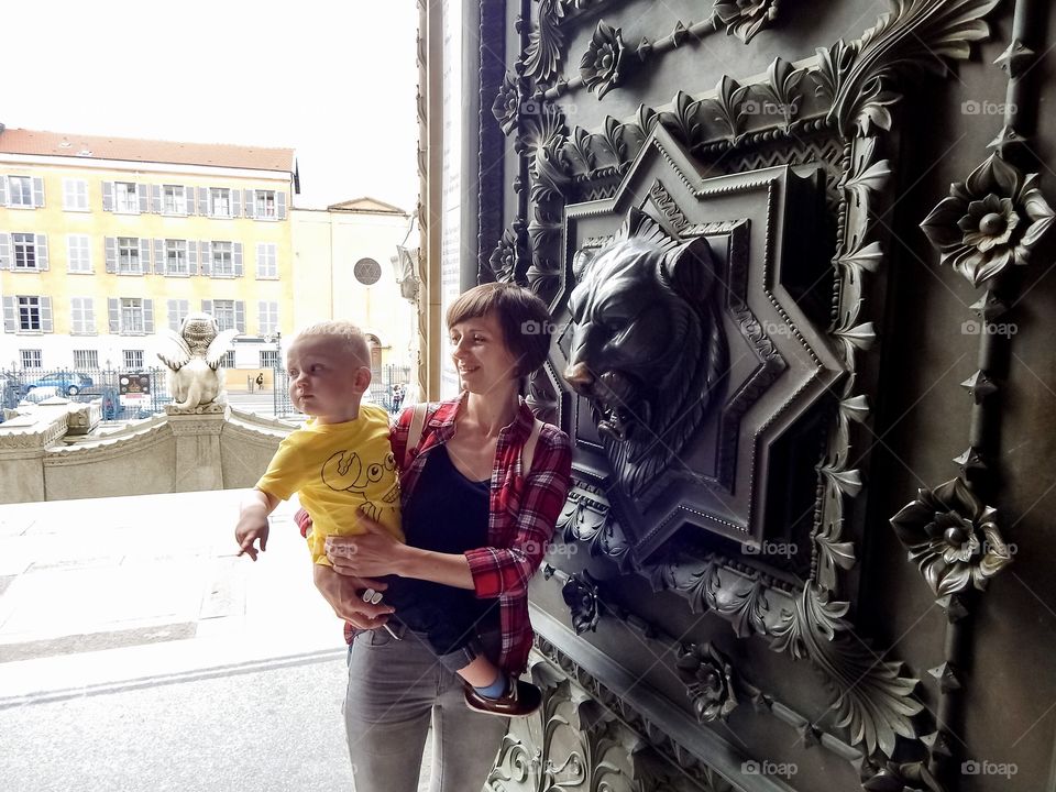 woman holds in her arms a boy at the ancient door of the cathedral with the head of a lion
