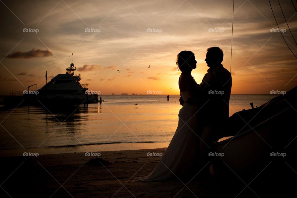 Beautiful couple on a tropical paradise watching the sunset go down waiting to take off on their yacht. 