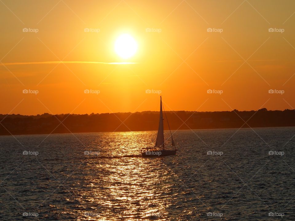 A sailboat passes through the sunsets reflection at Beavertail, RI.