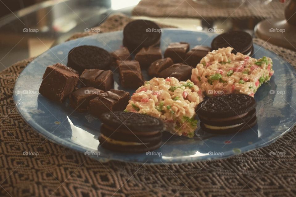 A snack plate of homemade rice crispy treats, oreos, and chocolate fudge pieces. 