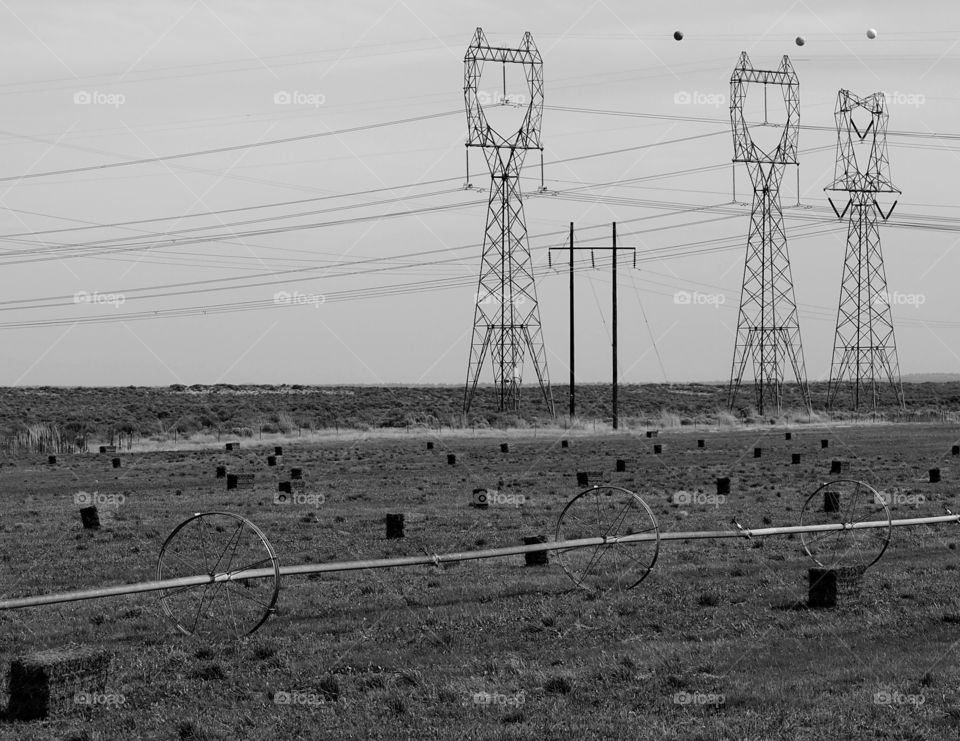 Giant electricity towers running through a field with freshly cut hay bales in Southern Oregon on a sunny fall day. 