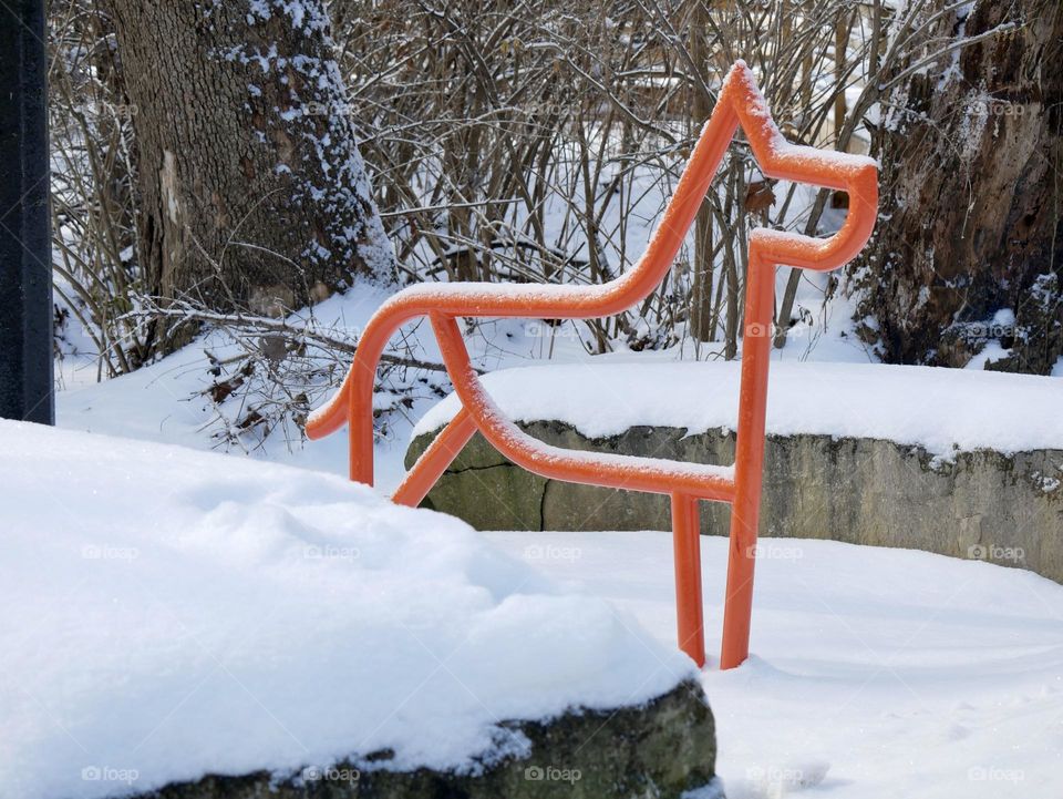 An orange metal dog in the snow, meant as a quick tie-off location for man’s best friend. 