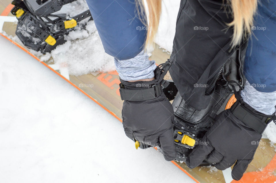 Close-up of a woman's gloved hands fastening a boot to a snowboard