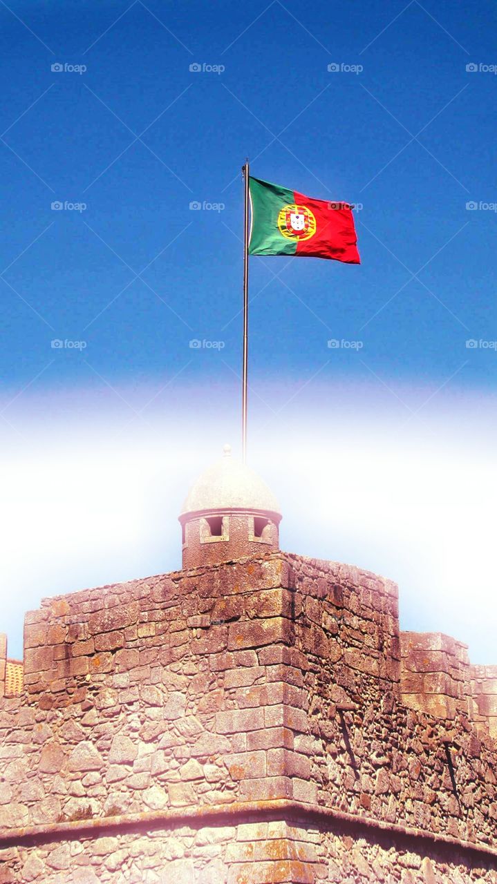 a castle on a beach with the Portuguese flag