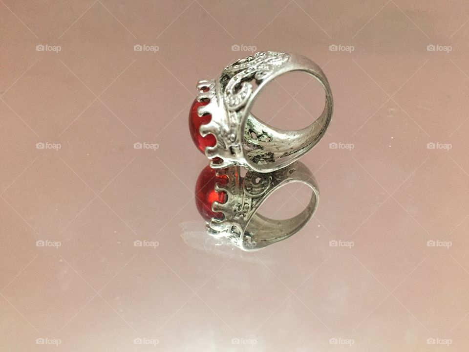 A silver ring with a red diamond in the middle reflected on a mirror