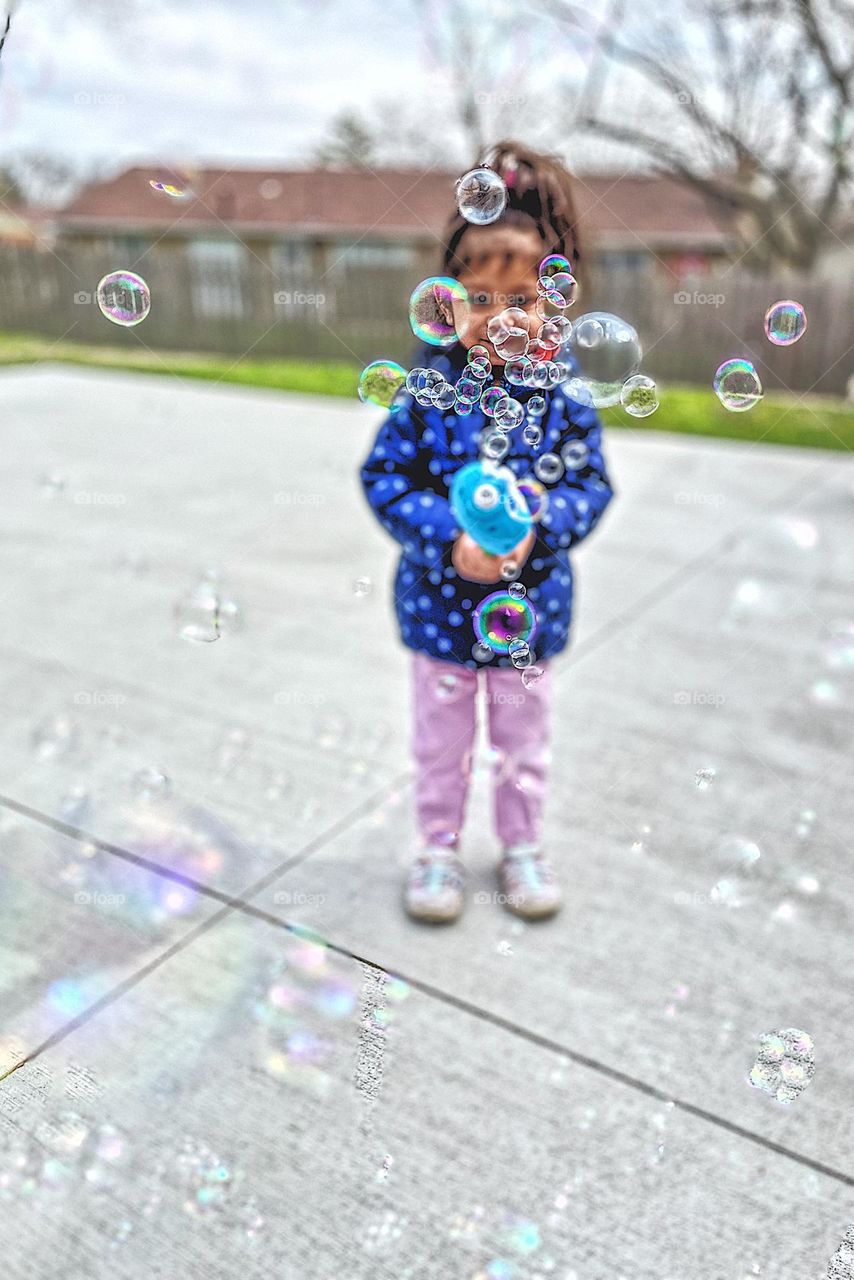 Toddler blowing bubbles outside, circular bubbles everywhere in frame, blowing bubbles with toddlers, circular items in everyday life, circles everywhere, toddlers playing outside, fun with bubbles, bubbles toy makes lots of bubbles, excited toddler