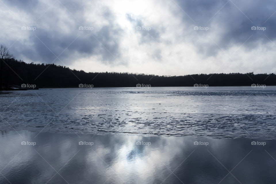 Partly ice covered lake on a grey winter day with dramatic clouds, reflections in the water 