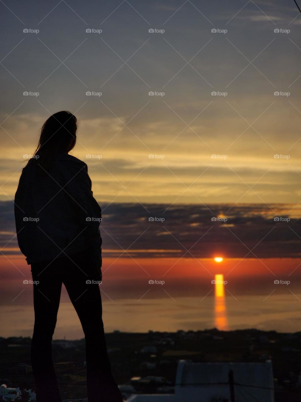 Early sunrise watching in Santorini, Greece. A girl watching the sun coming out with dramatic skies