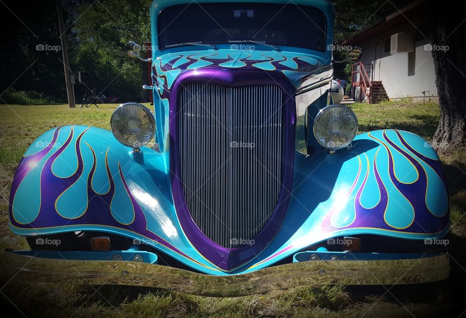 a classic hot rod displayed at a car show with beautiful purple flames  and purple around the grill. Notice the reflection on it low bumper