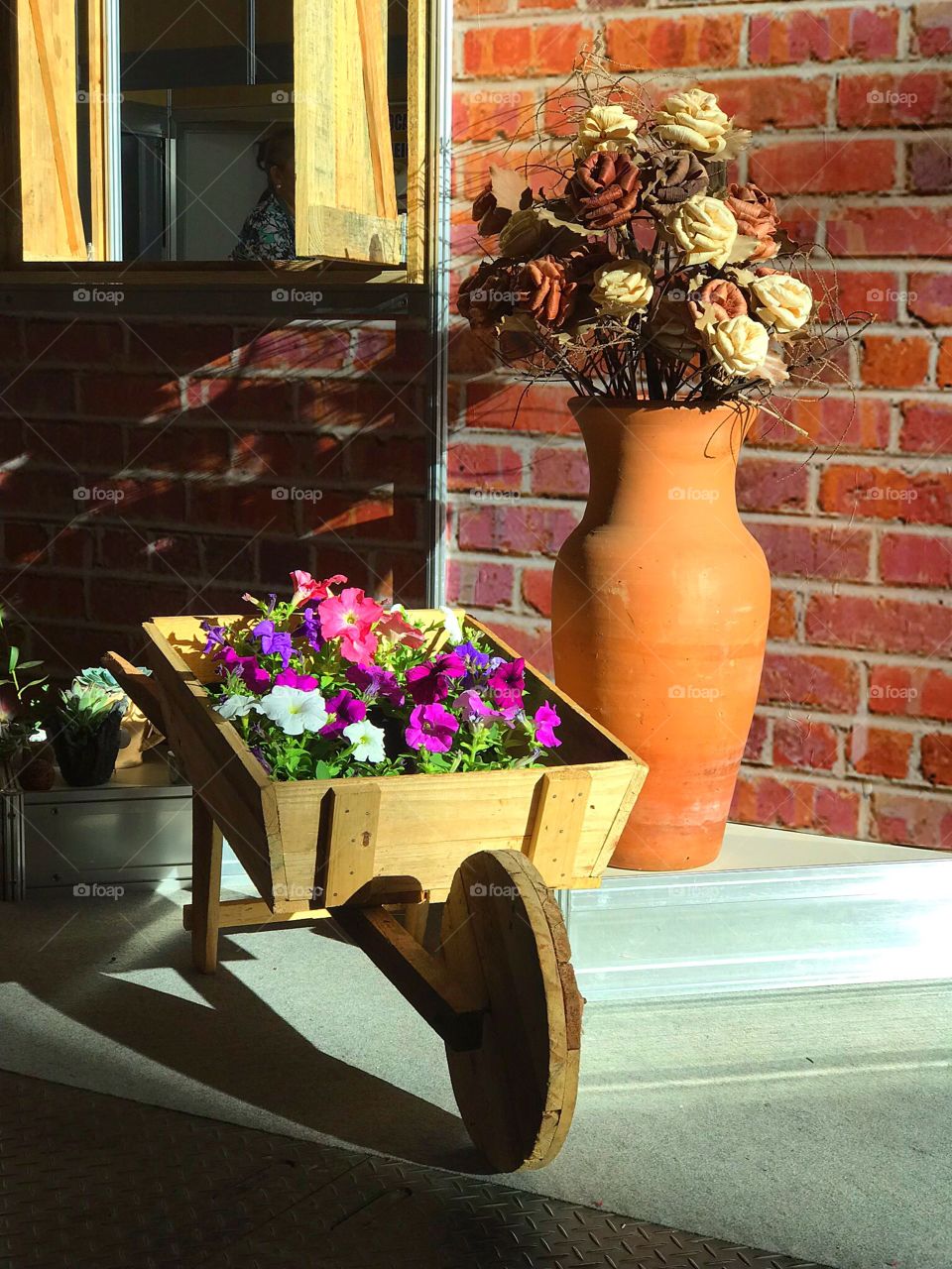 Colored Petunias in wooden hand cart and clay jug with dried handmade flowers.