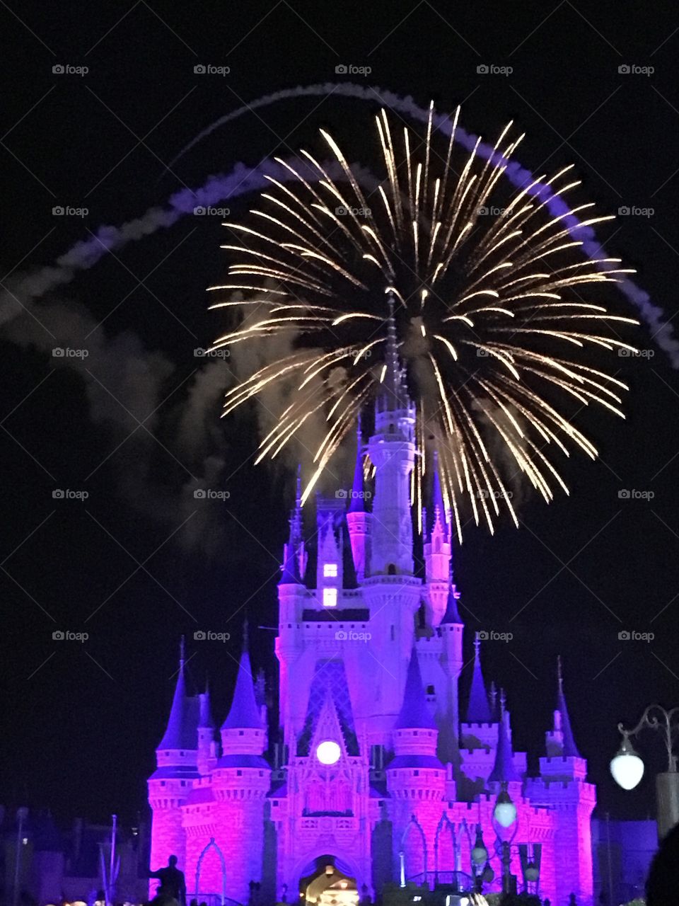 A beautiful picture of a large golden firework behind an illuminated purple Cinderella’s Castle, in Disney World 