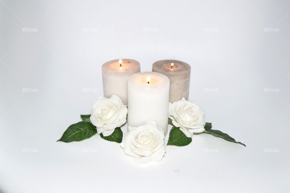 Lighted candles stone color with roses white green leaf on white background. 