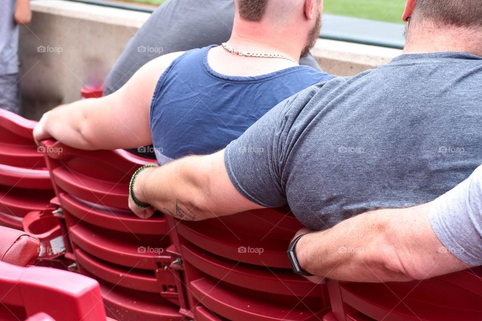 Row of people sitting in stadium seats with arms across the backs of the chairs 