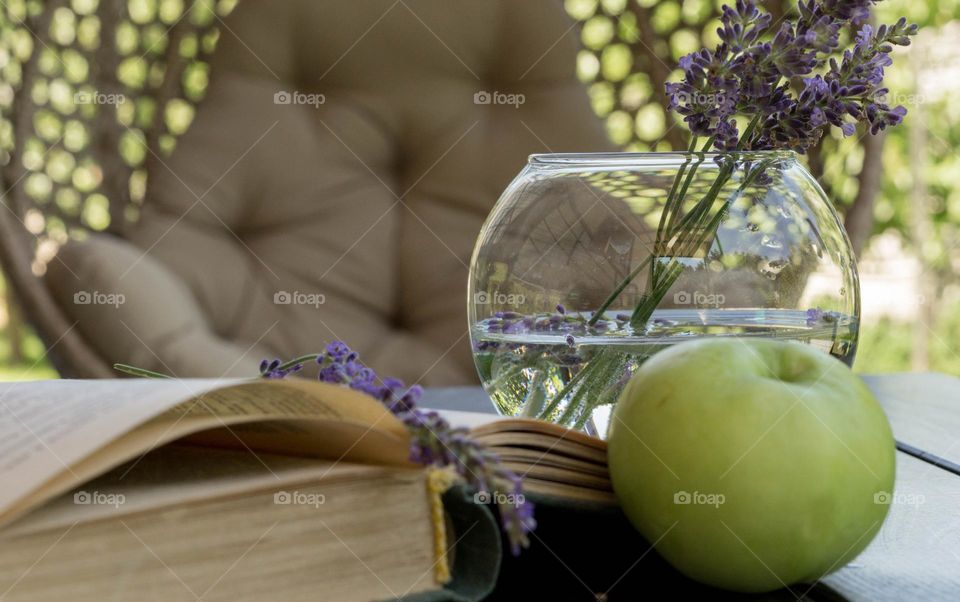 Flowers in a vase on a table, a book, an apple and relax chair 