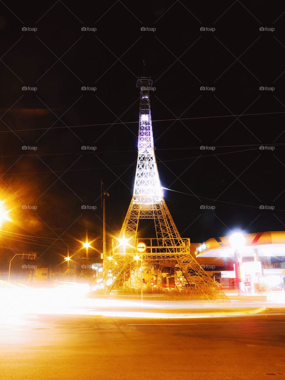 Long exposure light trails of a roundabout at night, with an Eiffel Tower model on the center