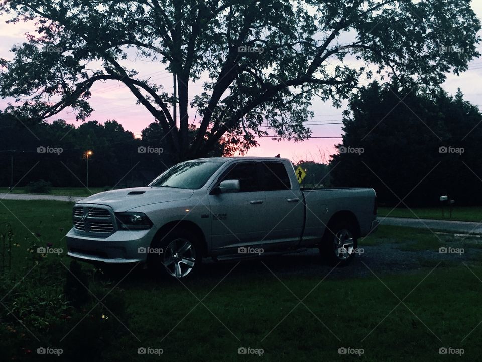 Silver Dodge Ram truck sitting in the driveway with a pink sky and tree silouhetted behind it, 