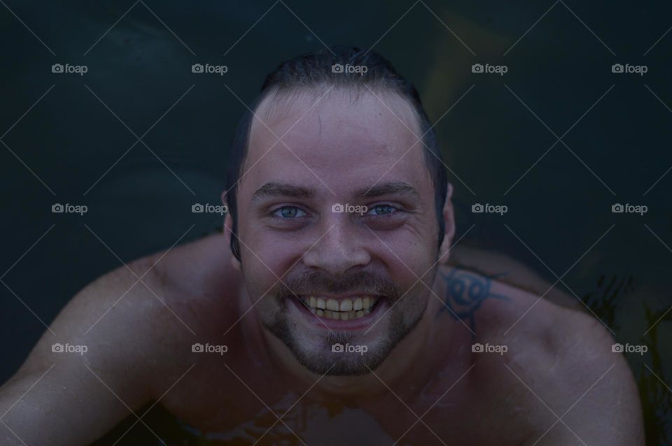 smiling man with cancer zodiac sign tattoo emerging from water.