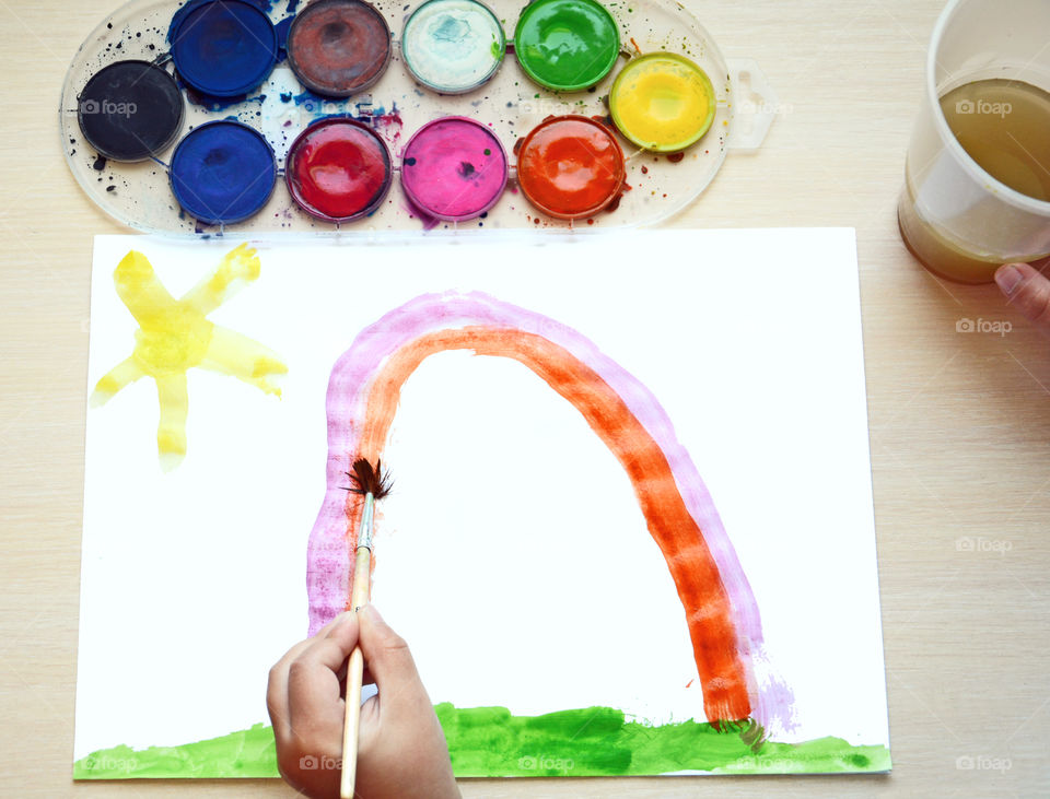 A little boy painting rainbow on paper