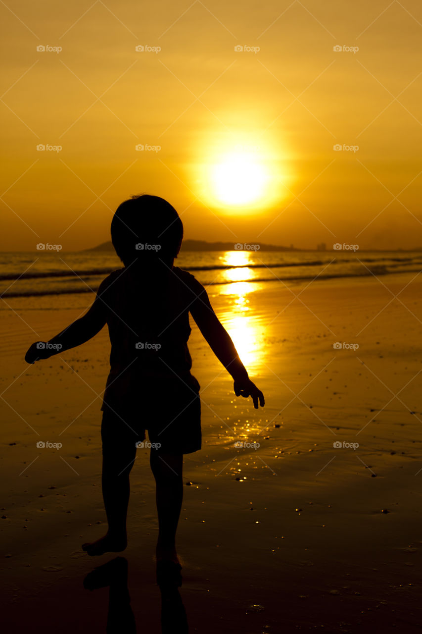 boy silhouette on the beach by the sea during sunset golden hour