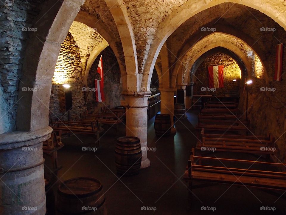 The beautifully designed cellar of Chateau dé Vianden in Luxembourg with grand arches, pillars, and flags. 