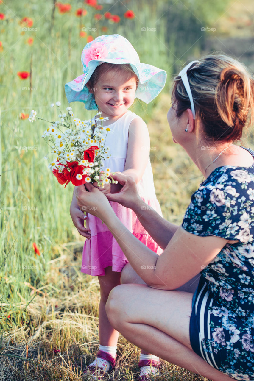 Mother and her little daughter in the field of wild flowers. Little girl picking the spring flowers for her mom for Mother's Day in the meadow. Girl handing the flowers to her mom. Nature scene, family time