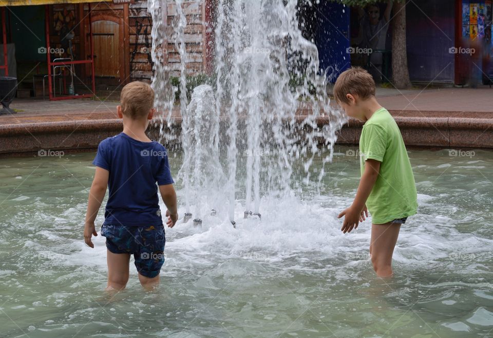 children boys in the water splash fountain, summer heat, city street view
