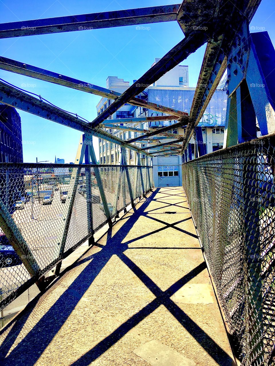 A walkway across a metallic structure overpass leading to Borden Avenue which runs parallel to the water of Newtown Creek in Long Island City, Queens. The photo was taken in the summer of 2019. Hypnotic Productions