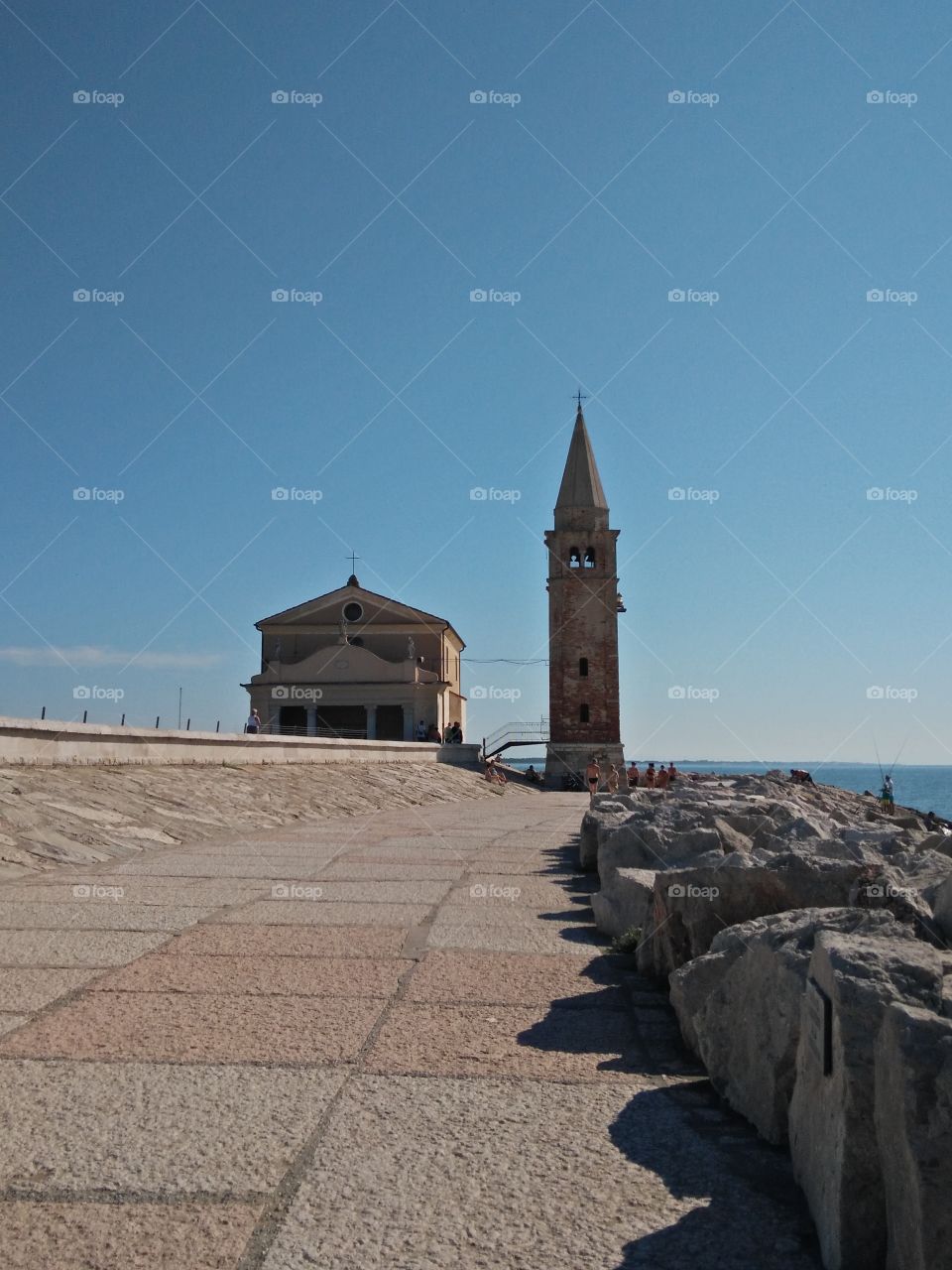 a panoramic view of madonna dell angelo church and the lighthouse bell tower in caorle venice italy seafront city cliff