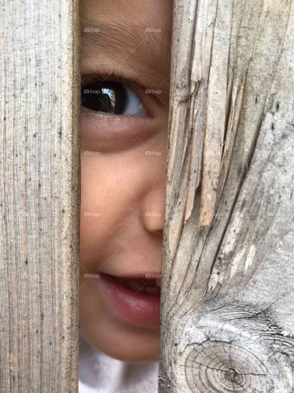 Young boy looking through the space between two wooden boards