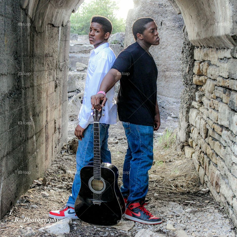 Two african man standing with guitar near stone wall