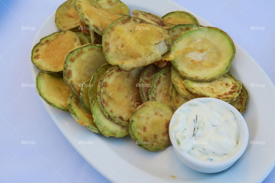 Fried zucchini chips with tzatziki Greek tavern plate. Floured zucchini are a dish commonly served at Greek tavernas, with a tzatziki sauce made of yogurt, cucumbers, salt, olive oil, and vinegar.