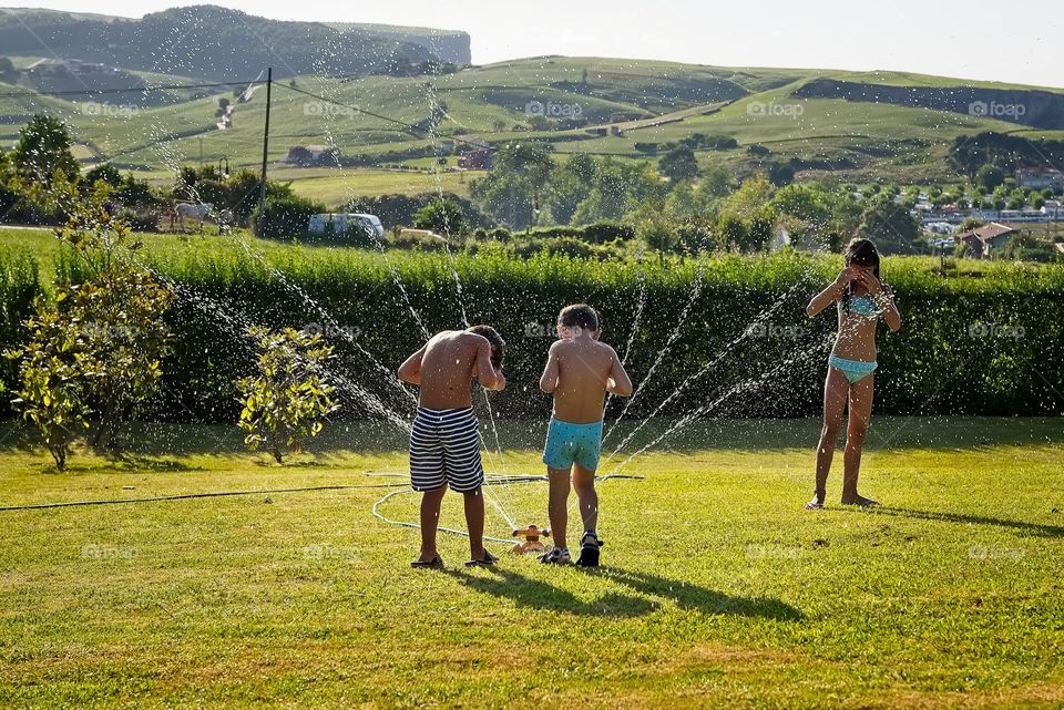 Children play with water sprinkler In the garden