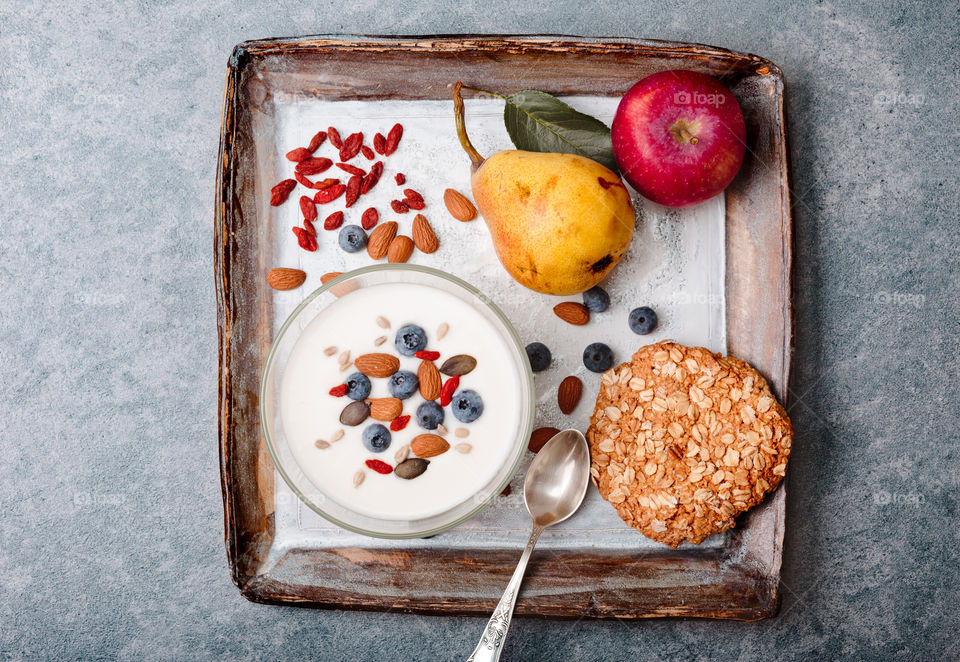 Breakfast on table. Yogurt with added blueberries and roasted almonds. Muesli cookie, apples and pears on table. Light and healthy meal. Good quality balanced diet. Flat top-down composition