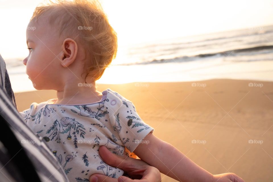 Close up of mother holding baby with sunrise beach on the background