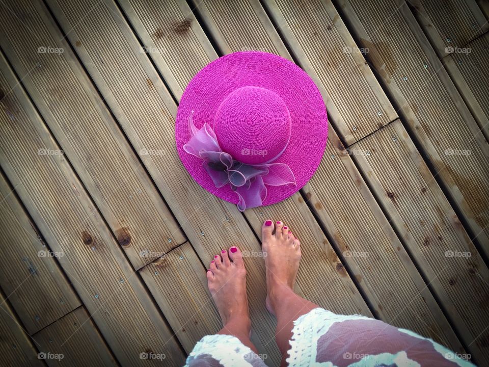 Looking down at woman wearing white dress standing near a pink summer hat on wooden pontoon