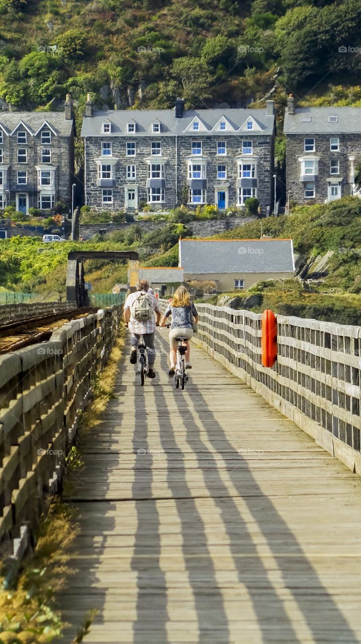 Rear view of man and woman cycling on wooden bridge